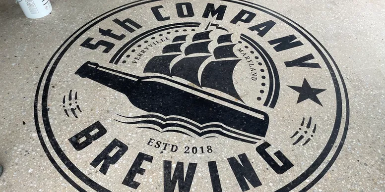 Custom stained concrete floor with 5th Company Brewing logo stencil